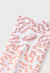 Λευκή κάλτσα αστραγάλου με υφή σε ανοιχτό ροδακινί και καφέ. Διαθέτει κεντρικό λογότυπο και διακριτικά γεωμετρικά σχέδια.