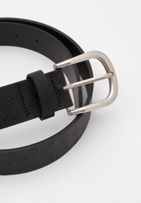 Sort læderbælte med en struktureret overflade, der har små præget prikker, fastgjort med en sølvfarvet metalspænde.