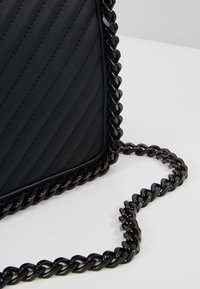 Mustakeroitu nahkabagi, jossa on punottu ketjusanka ja sileät reunat, sekä kohotettu vinoraita etuosassa.