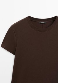 T-shirt marrone a maniche corte con scollo girocollo, colletto a costine e una piccola etichetta nera all'interno della scollatura.
