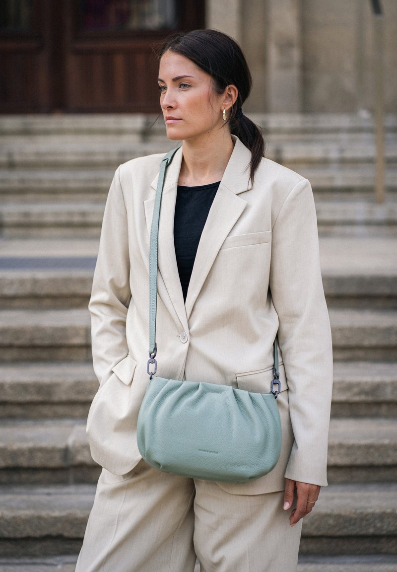 Weiche mintgrüne Leder-Crossbody-Tasche mit einem gerafften Design, verstellbarem Tragegurt und dezentem eingeprägtem Logo. Glatte Oberfläche, kompakte Form.