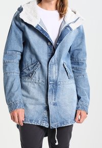 Blue denim jacket with a sherpa-lined hood, button closures, two front pockets, and drawstring hem. Features a faded wash and textured fabric.