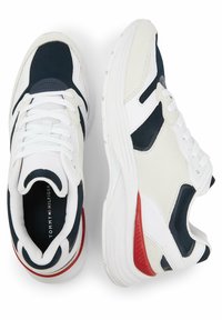 Zapatillas deportivas blancas y azul marino con materiales de malla y ante, acentos rojos en el talón y un diseño de suela gruesa. Los cordones son blancos.
