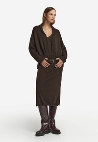 Mörkbrun oversized cardigan med knappar, kombinerad med en matchande figurnära kjol och knähöga burgundyskinnstövlar, som har ett texturerat bälte.