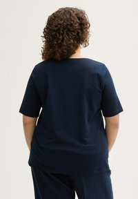Chemise à manches courtes bleu marine avec un col rond, présentant une texture lisse et une coupe décontractée, associée à un pantalon à rayures.