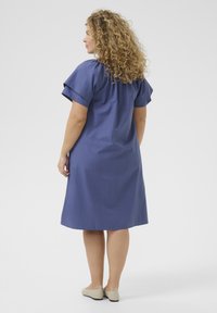 Blaues Baumwollkleid mit kurzen Ärmeln, lockerer Passform, knielang und einfachem Design. Getragen mit hellbeigen Slippern.