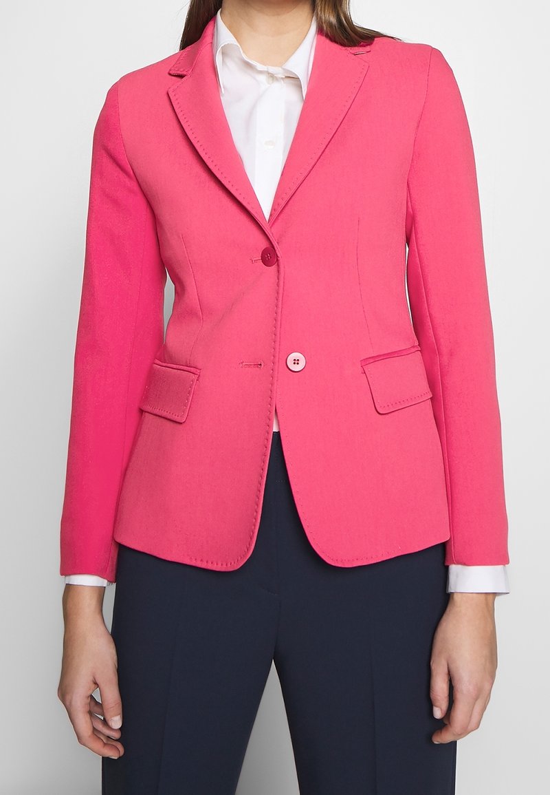 Blazer rose avec un design ajusté, deux poches avant et une fermeture à bouton unique. Présente une texture lisse et des coutures contrastantes.
