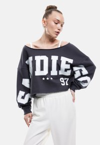 Czarny skrócony sweatshirt z białym nadrukiem graficznym i gwiazdkami, luźny krój, opuszczone ramiona, połączony z białymi spodniami na gumce.