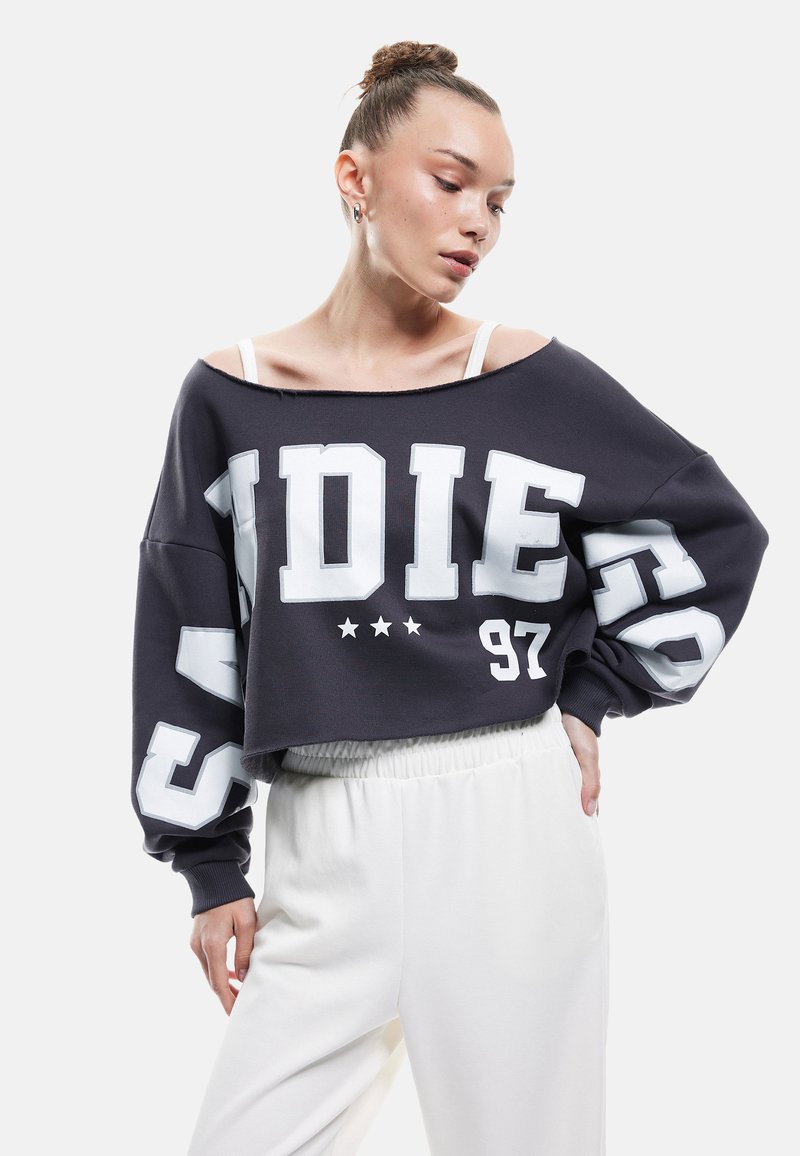 Czarny skrócony sweatshirt z białym nadrukiem graficznym i gwiazdkami, luźny krój, opuszczone ramiona, połączony z białymi spodniami na gumce.
