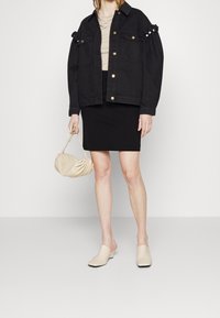 Chaqueta de mezclilla negra con botones dorados, blusa beige, falda negra, bolso crema con pliegues y mules beige claro con punta cuadrada.