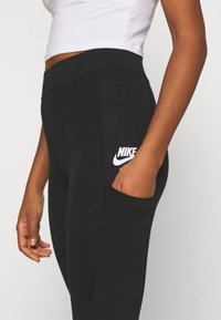 Svarta Nike leggings med hög midja, med en sidoficka och en vit Nike-logotyp. Materialet är mjukt och elastiskt.