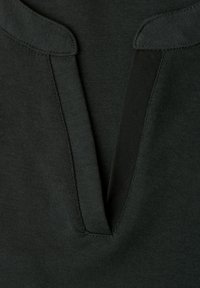 Gros plan d'un col en tissu vert foncé avec un décolleté en V et des détails de couture visibles.