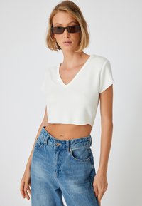 Hvid cropped t-shirt med V-hals og korte ærmer, sat sammen med højtsiddende blå denim jeans med klassisk knaplukning og lommer.