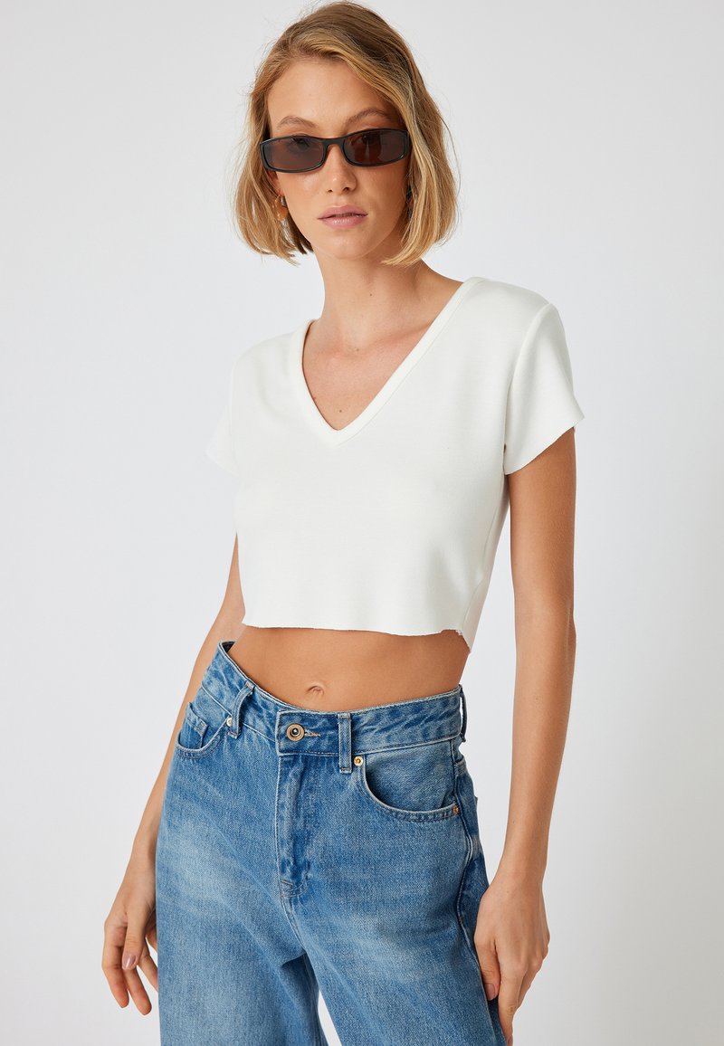 Hvid cropped t-shirt med V-hals og korte ærmer, sat sammen med højtsiddende blå denim jeans med klassisk knaplukning og lommer.
