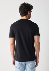 T-shirt en coton noir à manches courtes et col rond, vu de dos ; associé à un jean en denim décoloré.