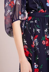 Blusa de seda azul marino con manga de estampado floral combinada con una falda azul marino que presenta patrones florales en rojo, blanco y verde, y cintura fruncida.