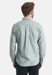 Lange mouwshirt van lichtgroene stof, met een traditionele kraag, knoopmanchetten en een plooi aan de achterkant voor extra bewegingsvrijheid.
