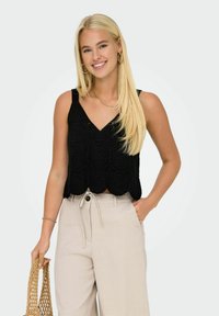 Top corto nero con design a orlo scallop, caratterizzato da un motivo floreale testurizzato. Abbinato a pantaloni high-waisted beige chiaro.