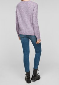 Lawendowy sweter z dzianiny o luźnym kroju, z prążkowanym wykończeniem na dole i ozdobionymi rękawami. Zestawiony z niebieskimi obcisłymi dżinsami i czarnymi botkami za kostkę.