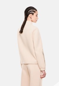 Pullover beige con collo alto e spalle drop, caratterizzato da dettagli testurizzati sulle maniche. Tessuto morbido con un design pulito e minimale.