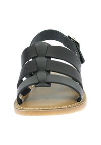 Sandalia de cuero negro con tres correas anchas, hebilla ajustable y suela plana color tostado. Presenta una textura suave y un diseño minimalista.
