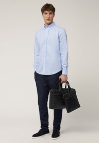 Lichtblauw button-up shirt, donkerdenim broek, zwarte leren tas met dubbele handvatten en zwarte sneakers met witte zolen.