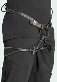 Černý horolezecký postroj s nastavitelnými popruhy, kruhovým kovovým kroužkem a kapsou se zipem. Textura je hladká a má odolný vzhled.