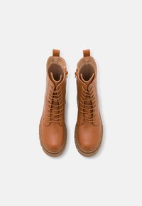 Botas de tornozelo em pele castanha com um acabamento suave, apresentando um fecho com atacadores à frente, um zip lateral e uma sola de borracha grossa.