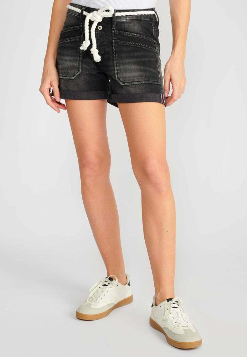 Shorts en denim noir avec taille à cordon, poches avant et ourlets roulés, associés avec des baskets blanches et grises avec des semelles en gomme.