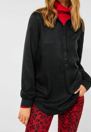 Blusa nera a maniche lunghe con colletto abbottonato, texture liscia, abbinata a pantaloni rossi con stampa leopardata, dal taglio slim e dotati di tasche.
