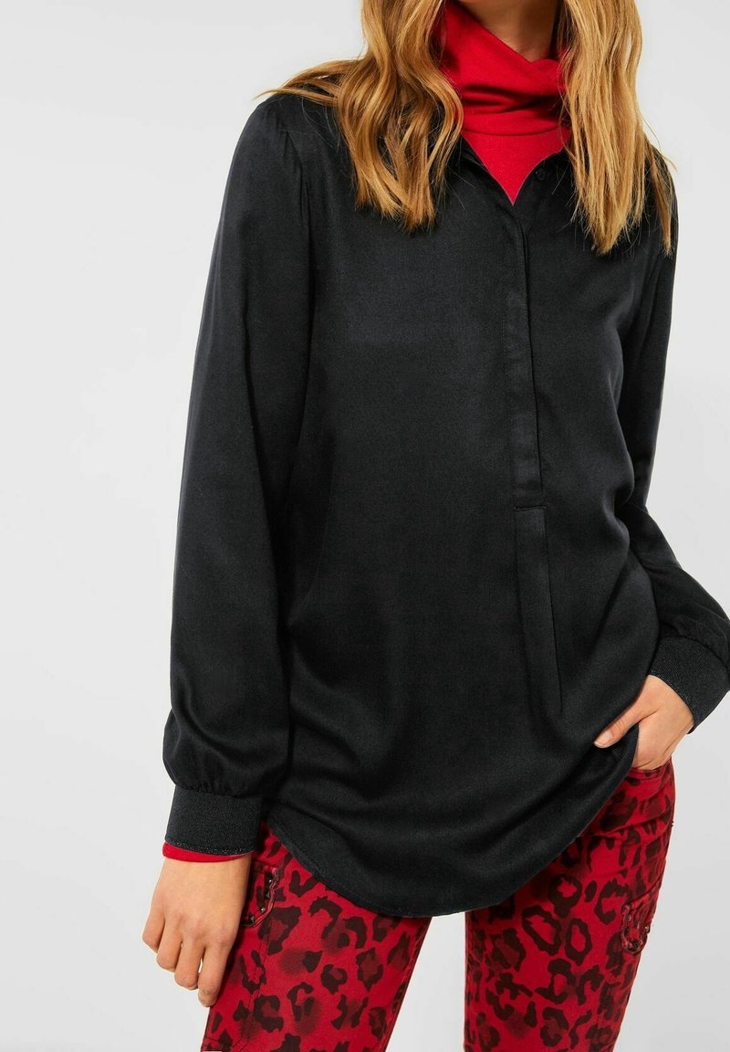 Zwarte blouse met lange mouwen en een knoopsluiting bij de kraag, gladde textuur, gecombineerd met rode panterprint broek met een slim fit en zakken.