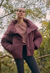 Burgundi värvi puffjakker laia krae, esiknappide ja veidi kortsulise tekstuuriga, koos helesinise sweatshirt'i ja mustade retuusidega.