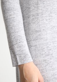 Grå texturerad tyg med ett subtilt prickigt mönster. Har en figursydd silhuett och en lång ärm med en ren finish vid manschetten.