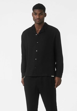 Sort, langærmet skjorte med knapper i tekstureret stof, med spids krave og synlige knapper, kombineret med matchende sorte bukser.