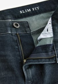 Slim fit donker denim jeans met een rits, metalen knoopsluiting en lichtblauwe voering met accentlijnen.
