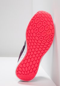 Sportovní bota s texturovaným černým svrškem a živou růžovou podešví s hexagonálním vzorem. Obsahuje bílé lemování podél podešve.