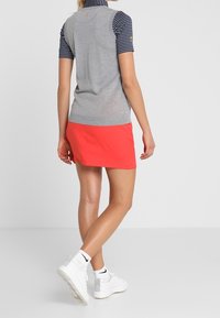 Haut gris sans manches avec col rayé bleu marine, associé à une jupe rouge vif. Chaussures blanches avec des accents gris. Design simple, style décontracté.