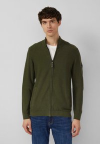 Olivengroene vest met rits, gemaakt van een gestructureerde brei, met geribde accenten aan de kraag en manchetten, voorzien van twee zakken aan de voorkant en een losse pasvorm.