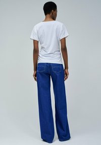 Camiseta de algodón blanca de manga corta, combinada con unos vaqueros de denims azules holgados con bolsillos traseros y un corte recto.