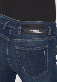 Mörkblå denimjeans med en kroppsnära design, med kontrasterande sömmar, en etikett märkt "PINKO," och bakfickor med subtilt slitage.