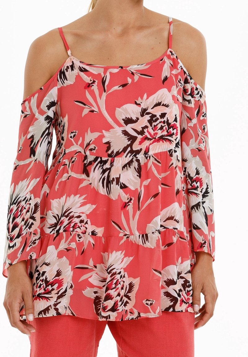 Blouse florale en corail avec des manches longues à épaules dénudées. Présente un design à volants, des motifs de fleurs noir et blanc, et des bretelles ajustables.