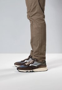 Buty sportowe z mieszanką brązowych, szarych i granatowych materiałów, z teksturowaną powierzchnią, białymi akcentami i masywną podeszwą.