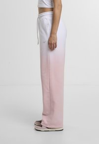 Lightweight, soft sweatshirt pants in a pink-to-white gradient. Features an elastic waistband and side pockets, paired with casual footwear.