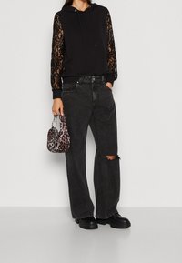 Felpa nera con maniche in pizzo, abbinata a jeans neri a gamba larga con un ginocchio strappato. Una piccola borsa a tracolla con stampa leopardata completa il look.