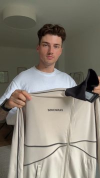 Μπεζ ζακέτα με φερμουάρ και μαύρο γιακά, με την ένδειξη "FRANCHISE" τυπωμένη σε μαύρο, και διακριτές καμπύλες ραφές.