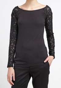 Černý dlouhý rukáv top s krajkovými detaily na rukávech, lodičkovým výstřihem a přiléhavým střihem. Měkká, elastická tkanina s hladkou texturou.