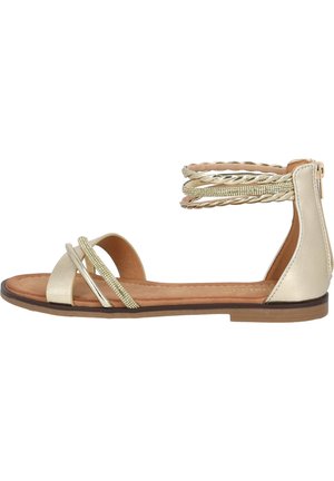 Flad sandal med metallic guld stropper, flettede og med rhinsten detaljer, polstret tan indersål og lynlås bagpå på en brun sål.