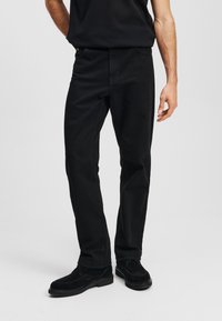 Pantalones de algodón negros con un corte recto, que presentan un diseño clásico de cinco bolsillos y detalles de costura sutiles, combinados con zapatos negros.