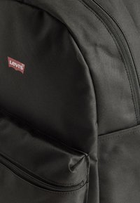 Zwarte Levi's rugzak met zichtbare voorzak met rits en close-up van de textuur van de stof.