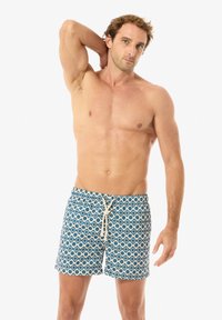 Bañadores de hombre con un patrón geométrico en azul y blanco, cintura elástica y cordón. Largo hasta el muslo, fabricados en tejido ligero.